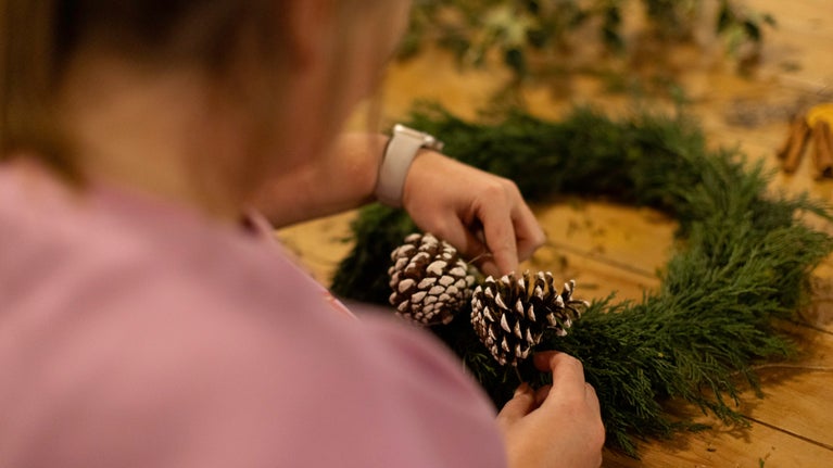 A visitor making a wreath with natural materials on a wooden table